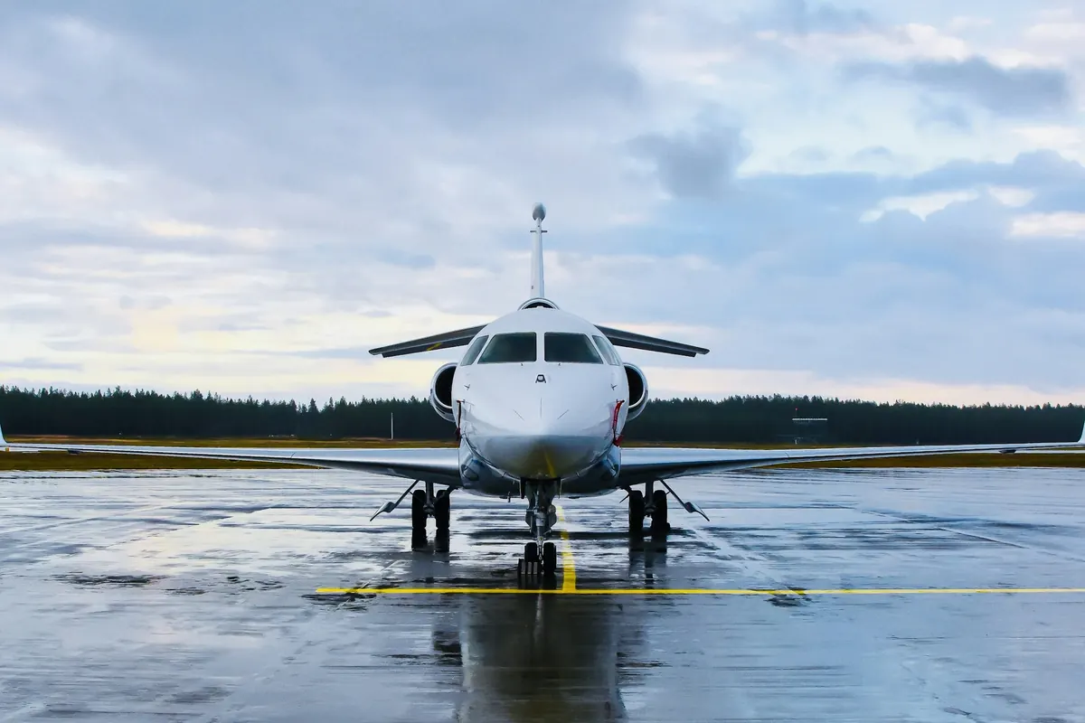 Large-cabin business jet parked on a wet ramp with pine forest behind