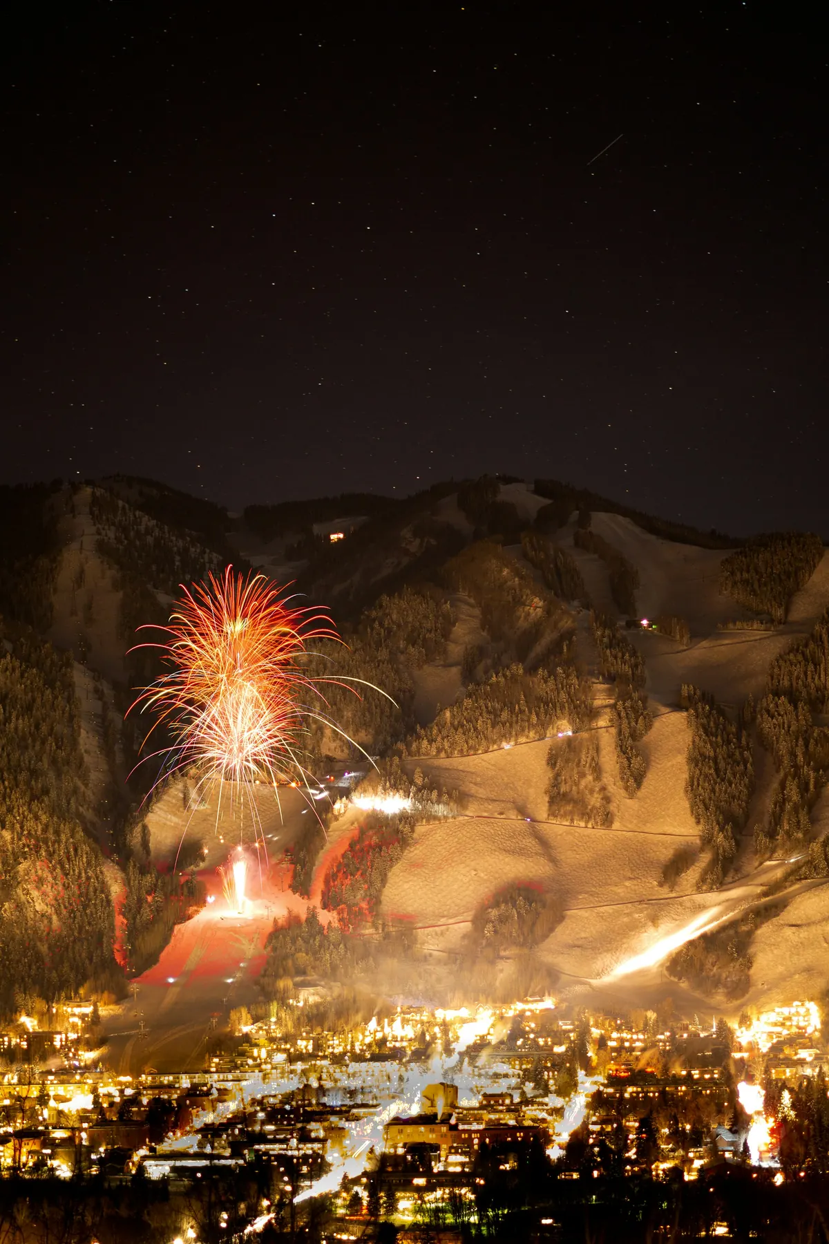 Fireworks over Aspen Mountain with the lights of town below on a winter night